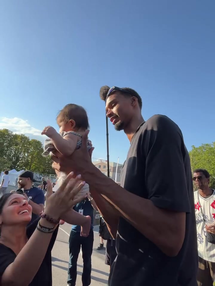 Victor Wembanyama holding a baby who tries to communicate with him